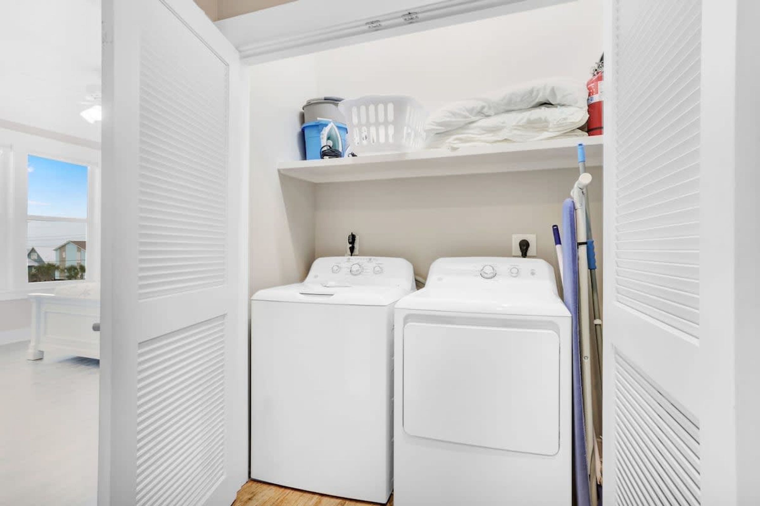 A laundry room with two white washing machines, a shelf with laundry supplies, and a mop leaning against the wall.