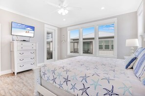A bedroom with a bed, a dresser, a TV, and a window with a view of buildings. - Life s Porpoise A Steps From Beach Pool (Gulf Shores)