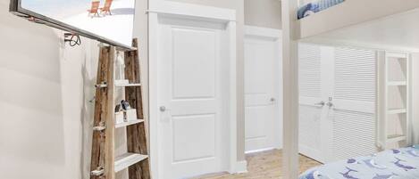 A bedroom with a bunk bed, a wooden shelf unit, a white door, and a wall-mounted TV displaying a beach scene.