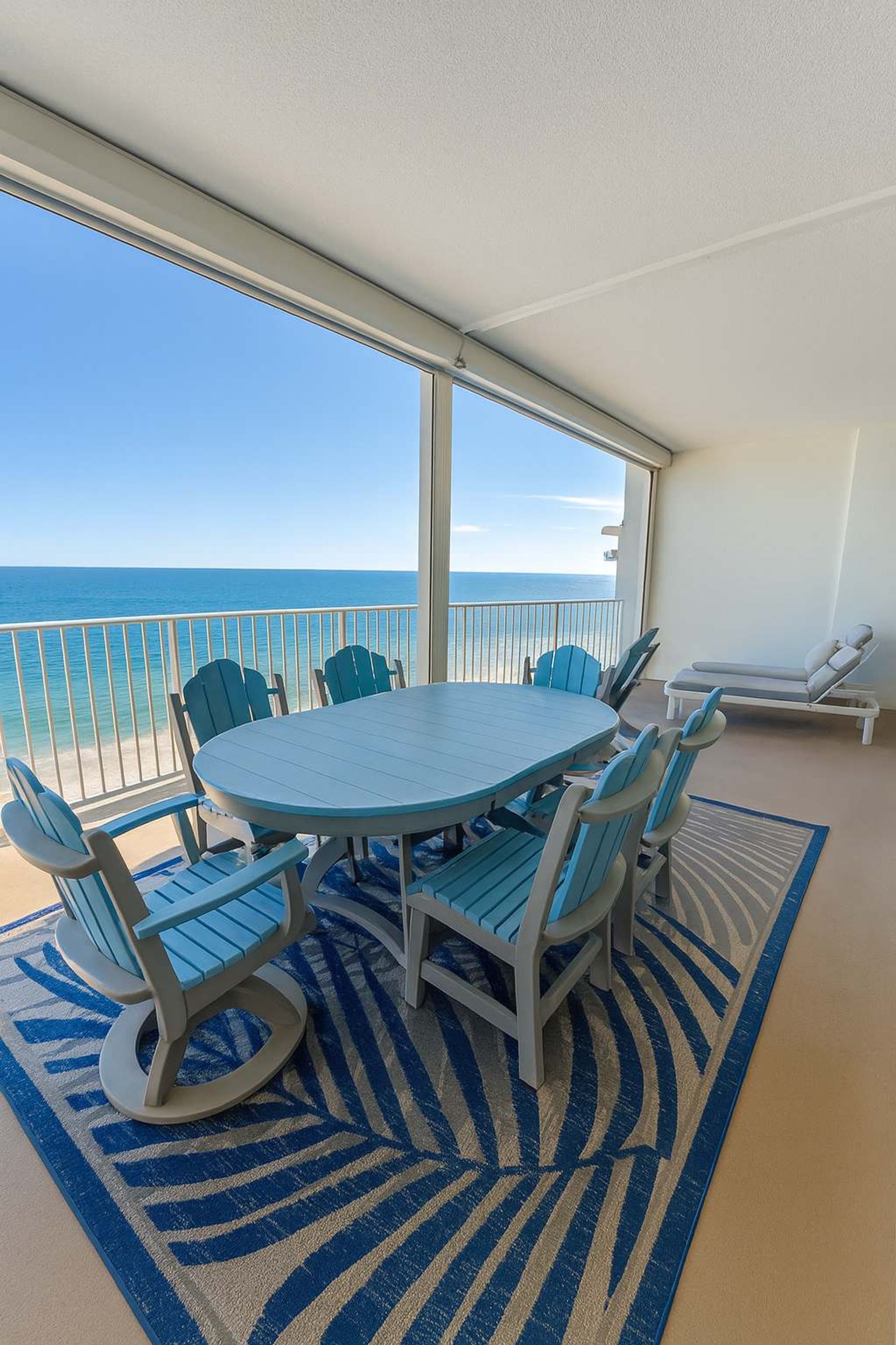 A balcony with a round table and chairs, a lounge chair, and a view of the ocean.