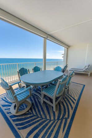A balcony with a round table and chairs, a lounge chair, and a view of the ocean. - Regency Isle Beachfront Bliss Amazing Views 2 Bedrooms (Orange Beach)