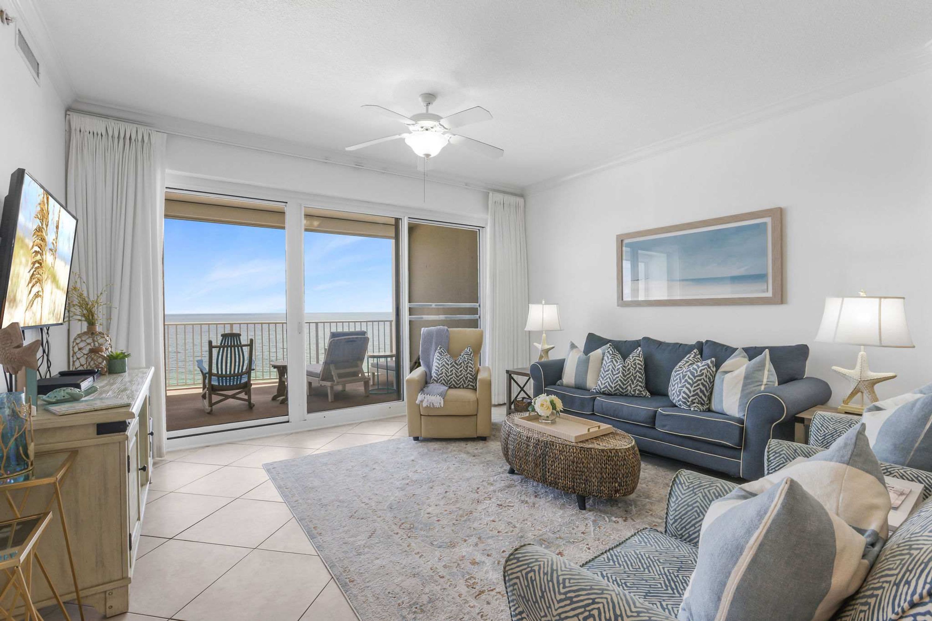 A spacious living room with a large sofa, a coffee table, and a balcony with a view of the ocean.