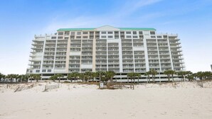 Ein mehrstöckiges Hotel mit flachem Dach, gelegen an einem Sandstrand mit Palmen im Vordergrund.