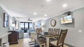 A spacious living area with a dining table, chairs, and a large window offering a view of the ocean. - Phoenix I 1112-11th Floor Splash pad Beachfront 2 Bedrooms 2 Baths (Orange Beach)