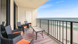 A balcony with wicker furniture and a table, overlooking a beach with waves. - Phoenix I 1112-11th Floor Splash pad Beachfront 2 Bedrooms 2 Baths (Orange Beach)
