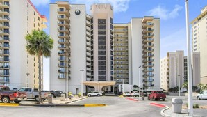 A multi-story hotel with a central entrance, balconies, and a parking area. - Phoenix I 1112-11th Floor Splash pad Beachfront 2 Bedrooms 2 Baths (Orange Beach)