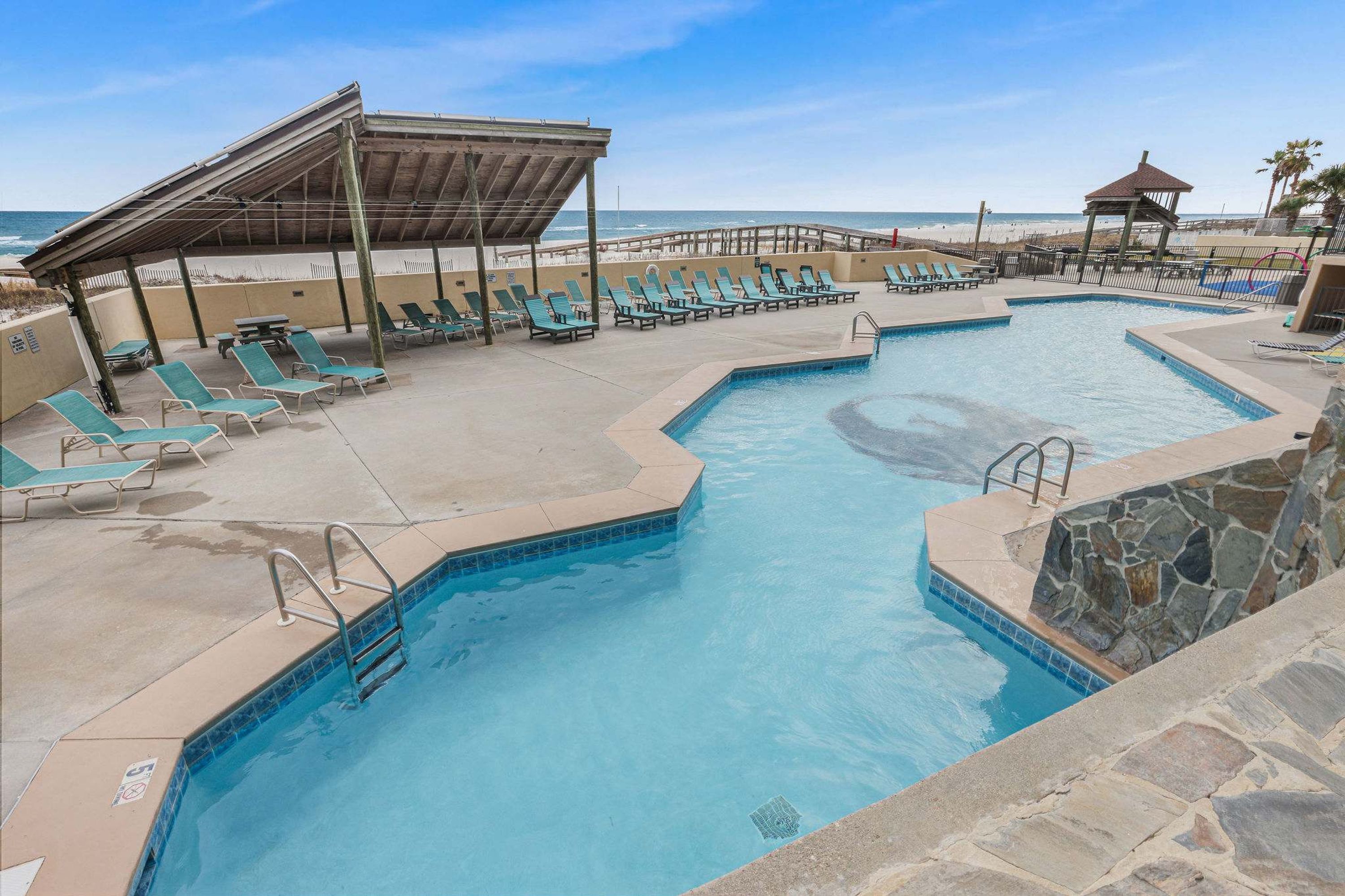 A pool area with lounge chairs and a covered seating area.