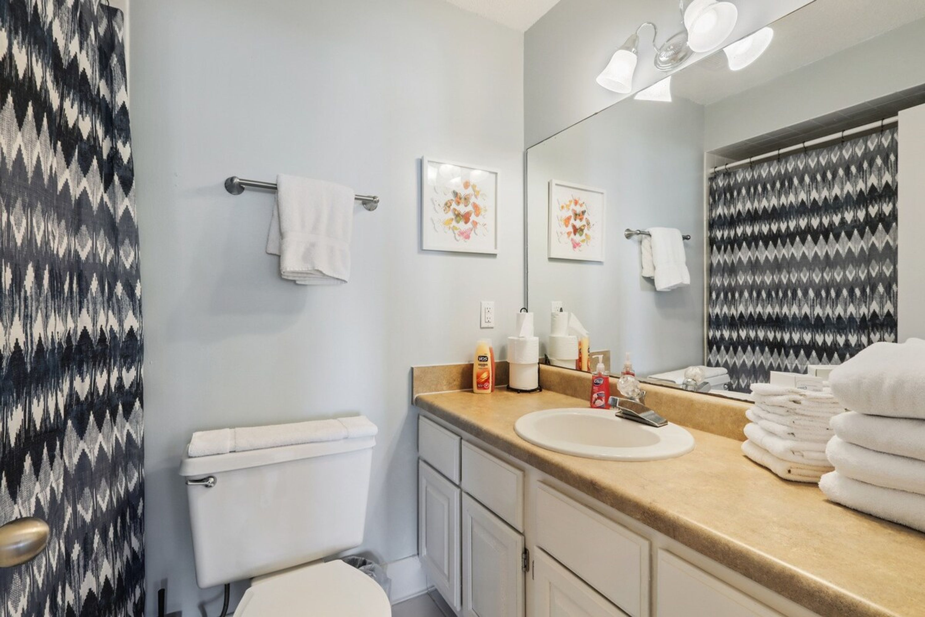 Une salle de bain avec des toilettes, un lavabo et un miroir. On y trouve des serviettes et des articles de toilette sur le comptoir.