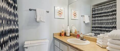 Une salle de bain avec des toilettes, un lavabo et un miroir. On y trouve des serviettes et des articles de toilette sur le comptoir.