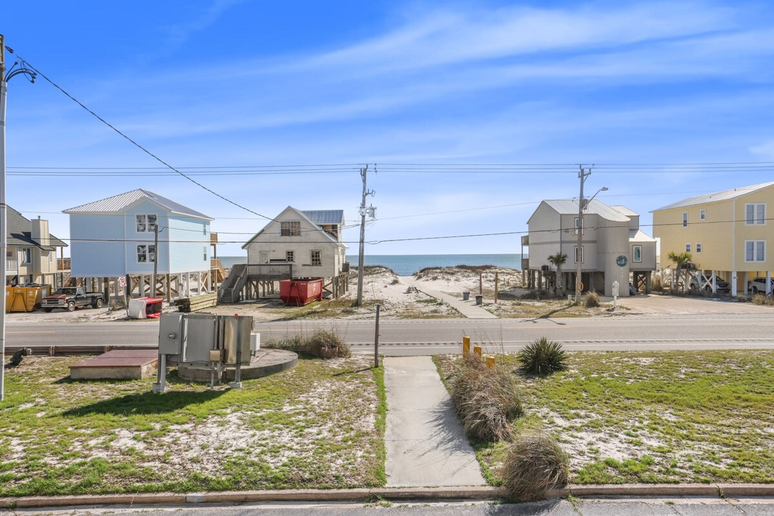 Una calle costera con casas, aceras y una playa al fondo.
