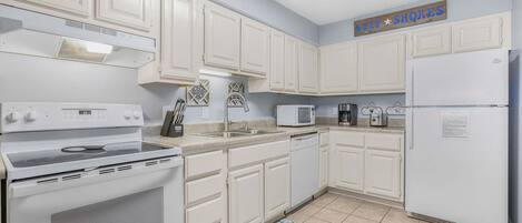 A kitchen with white cabinets, a stove, a microwave, and a refrigerator.