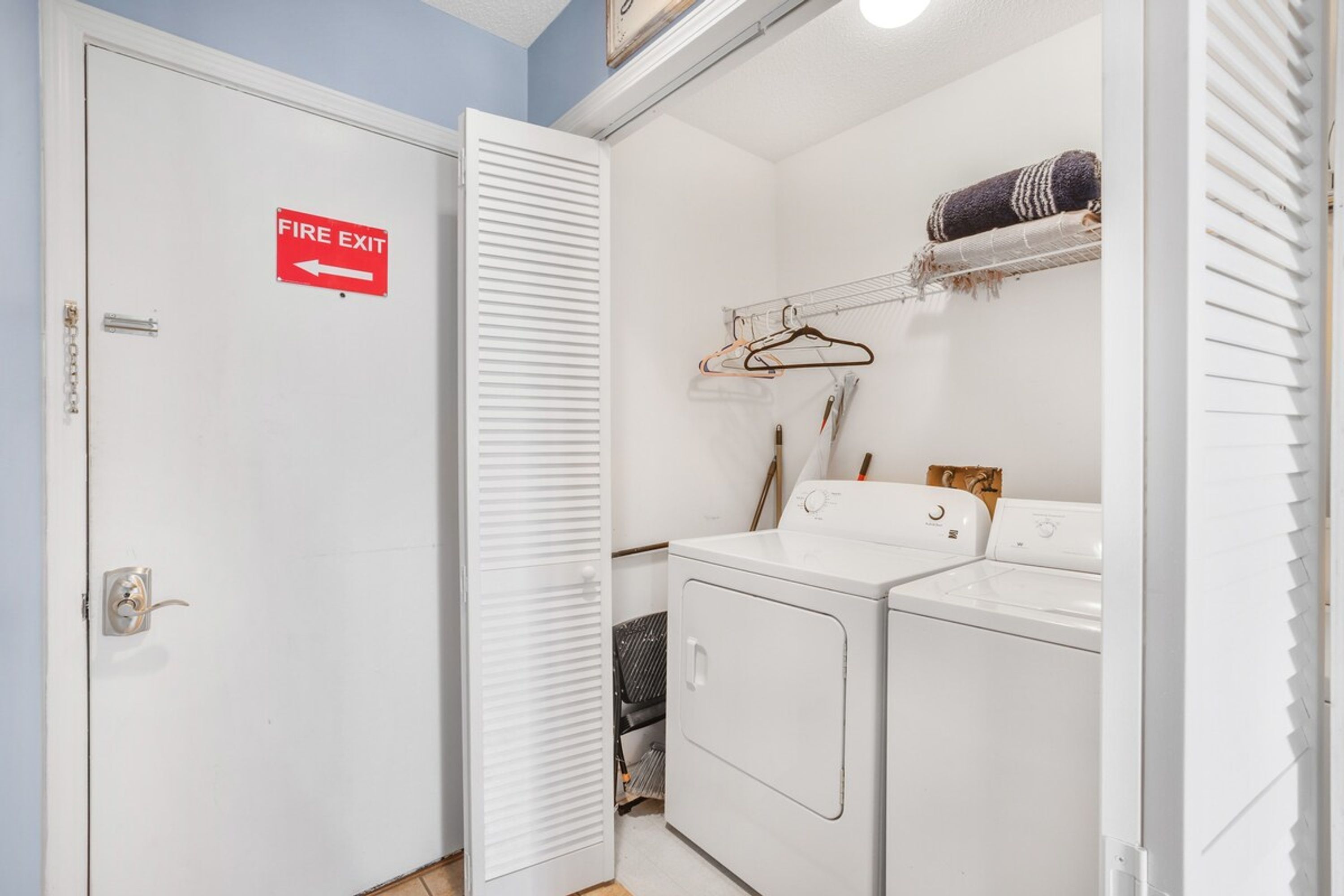 Uma lavanderia com placa de saída de incêndio, um varal e uma máquina de lavar roupa.