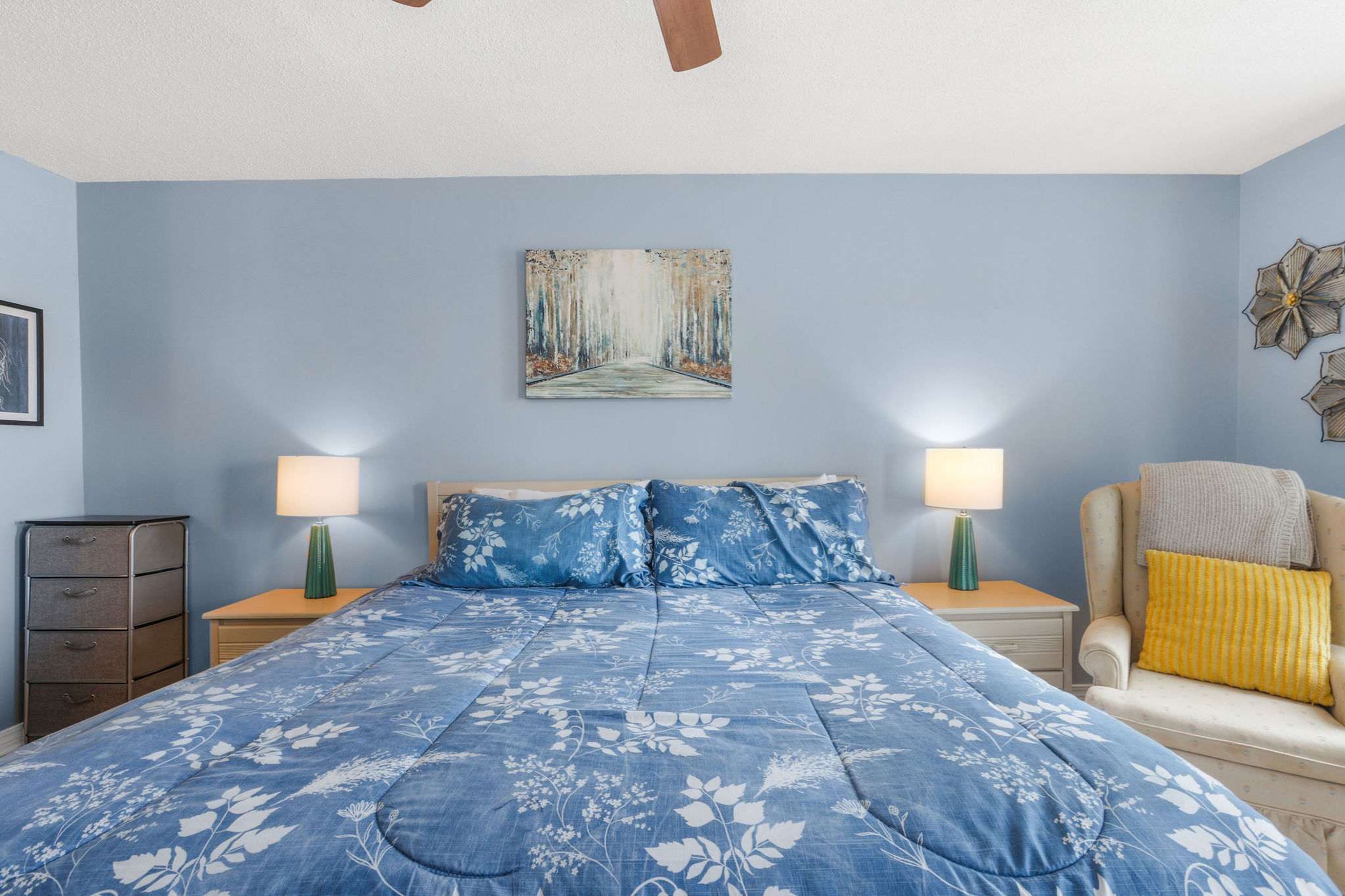 Une chambre à coucher avec un lit, deux tables de chevet, une chaise, une commode et un tableau au mur.