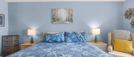 Une chambre à coucher avec un lit, deux tables de chevet, une chaise, une commode et un tableau au mur.