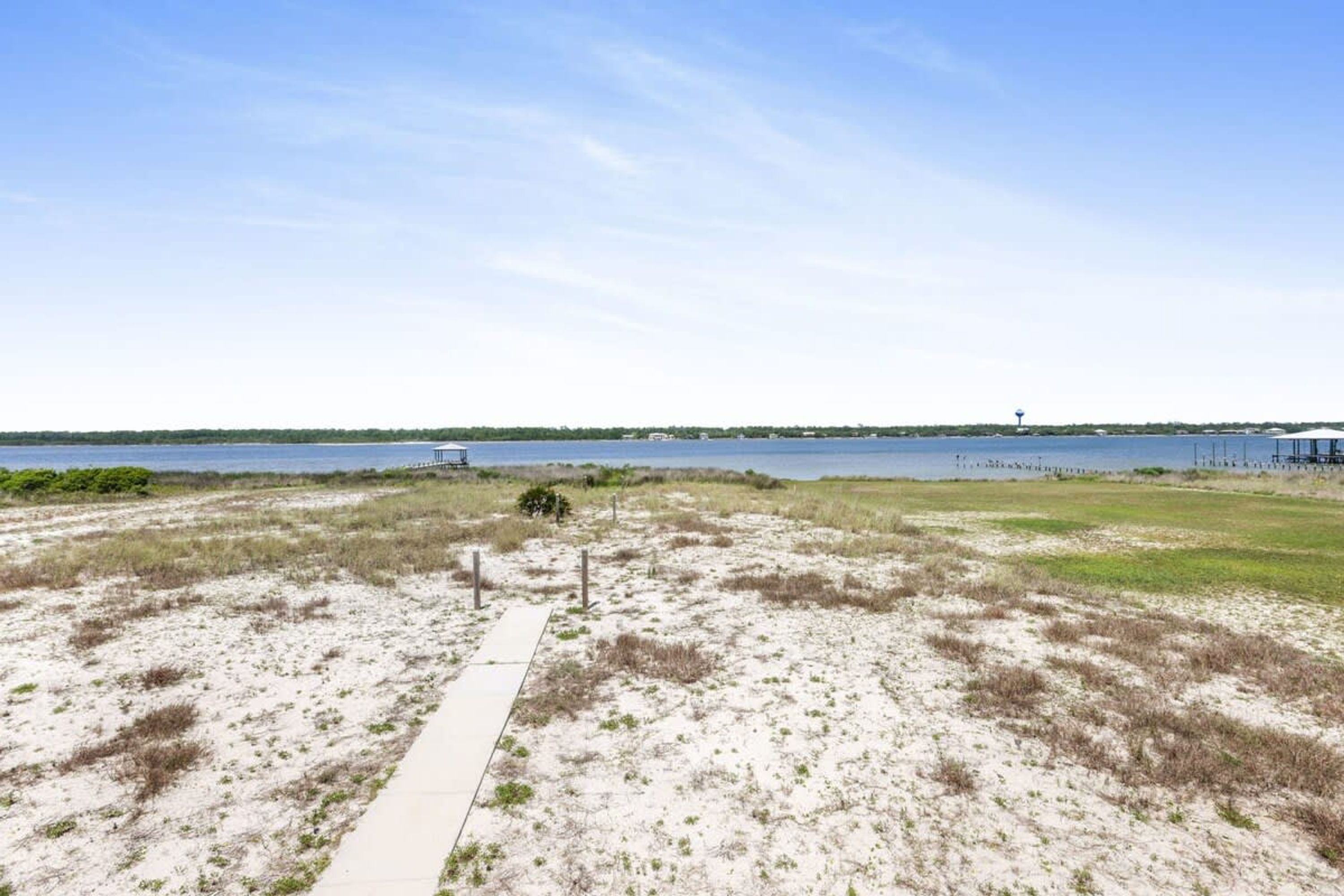 Ein Sandstrand mit einem Weg zum Wasser, einem entfernten Wasserturm und Gebäuden am Horizont.