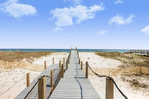 Une promenade en bois menant à la plage, entourée de sable et de dunes.