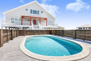 Un espace piscine avec une terrasse en bois, un bâtiment blanc doté d’une porte rouge et un panneau sur lequel on peut lire : « Cher Temps ».