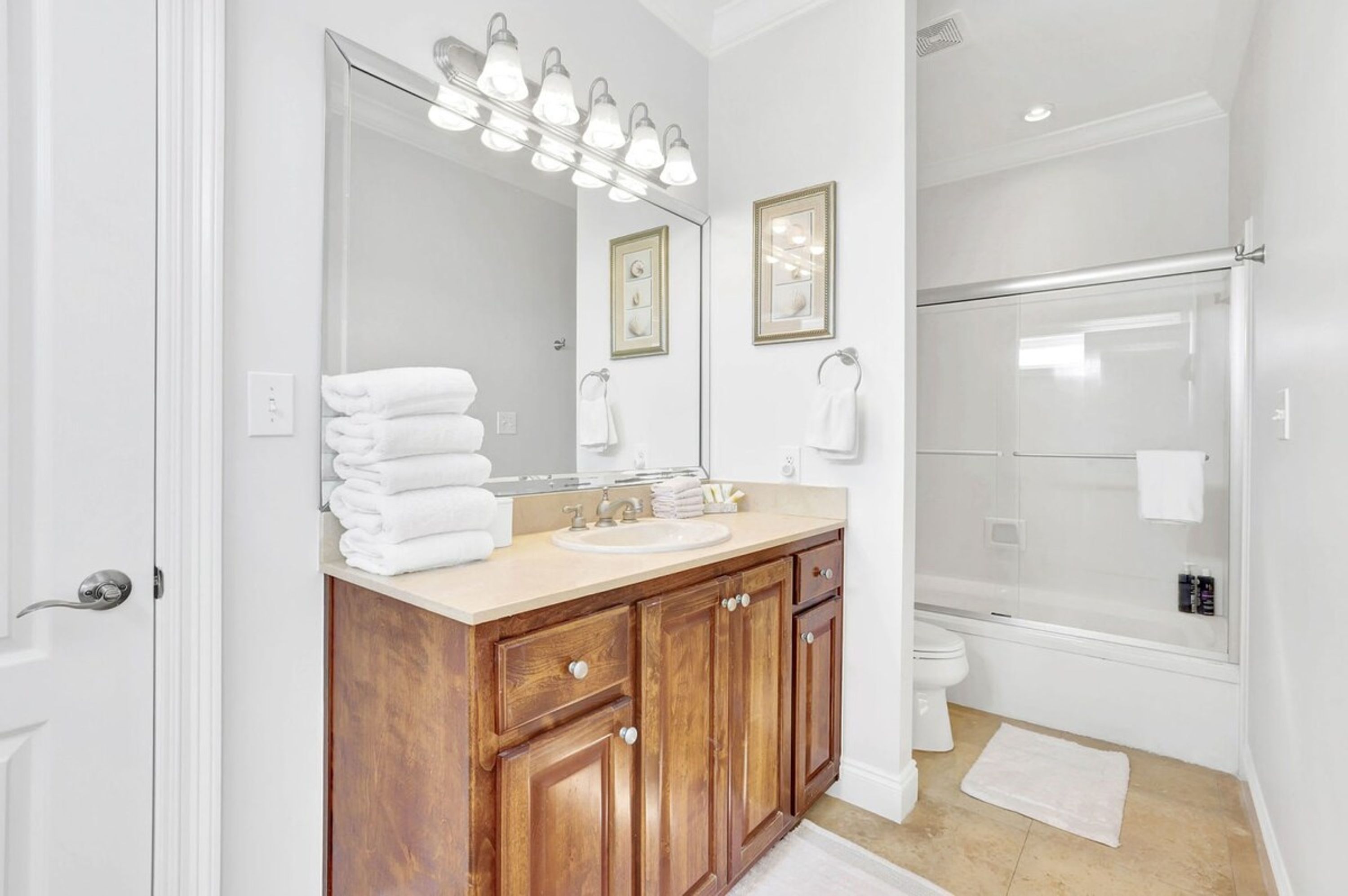 A bathroom with a wooden vanity, a large mirror with lights, a shower, and a toilet.
