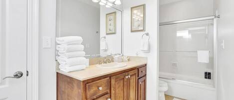 A bathroom with a wooden vanity, a large mirror with lights, a shower, and a toilet.