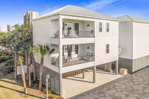 A two-story building with a balcony on the upper level, surrounded by palm trees. - Sweet Mama s 4 Bedrooms 4 Baths Cottage Beach Access Pool Sleeps 12 (Gulf Shores)