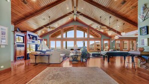 A spacious living room with wooden floors, a high ceiling, and large windows. - The Gayosa House 9BR Beachfront Oasis With Private Pool Hot Tub (Orange Beach)