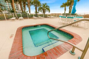 Una piscina rectangular con borde de ladrillo, rodeada de sillas reclinables blancas y una cerca blanca.