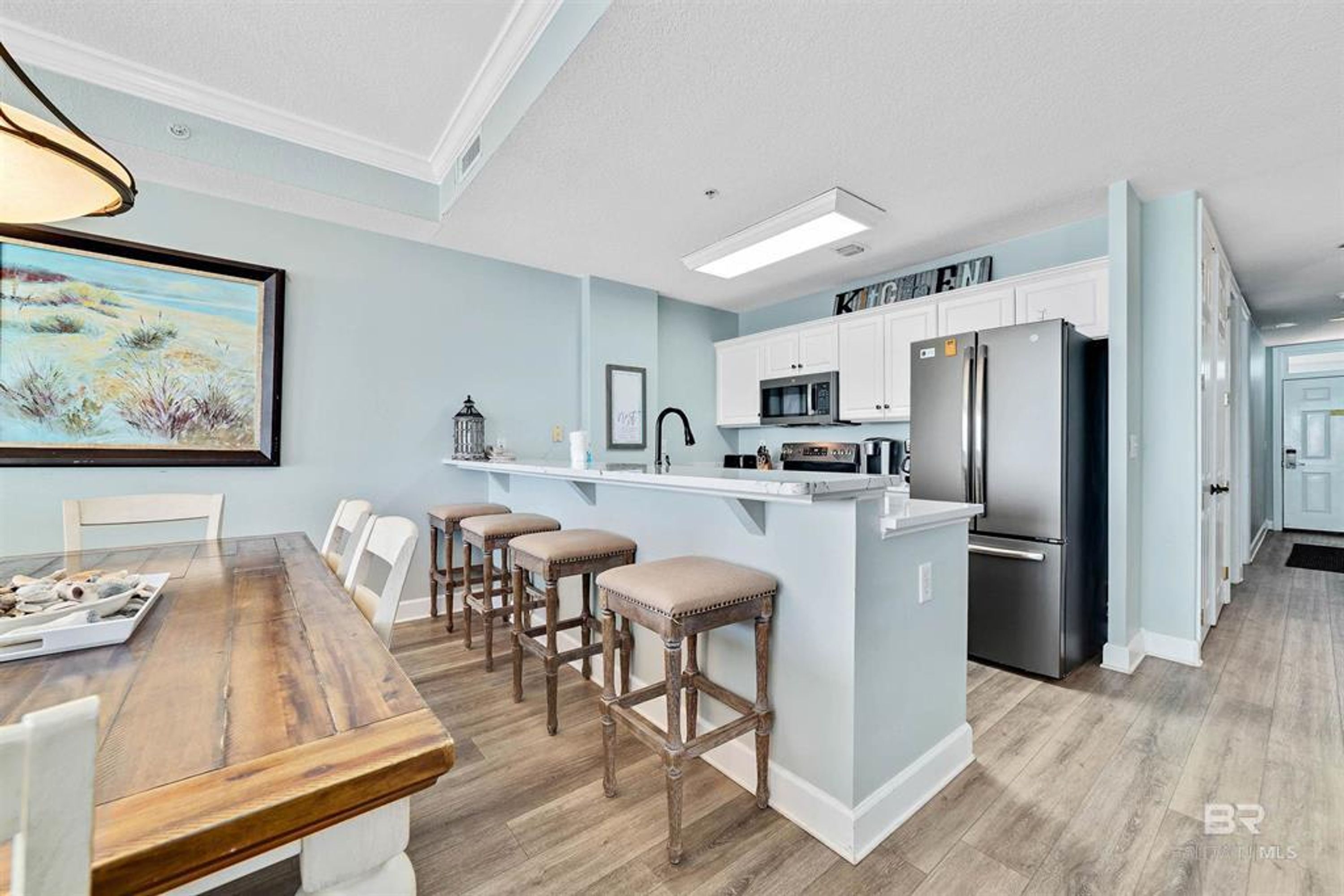 Una cocina moderna con armarios blancos, electrodomésticos de acero inoxidable y una mesa de comedor de madera con taburetes de bar.