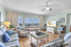 A living room with a view of the ocean, a ceiling fan, and a television. - Admirals Quarters 508- Luxury Beachfront Condo 3 Bedrooms 3 Baths 5th Floor (Orange Beach)
