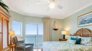 Een slaapkamer met een bed, een stoel, een bureau, een plafondventilator en uitzicht op de oceaan.