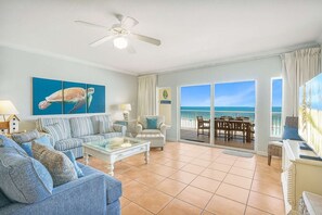 A spacious living room with a large window overlooking the ocean, a ceiling fan, and a dining area with a view. - Admirals Quarters 508- Luxury Beachfront Condo 3 Bedrooms 3 Baths 5th Floor (Orange Beach)