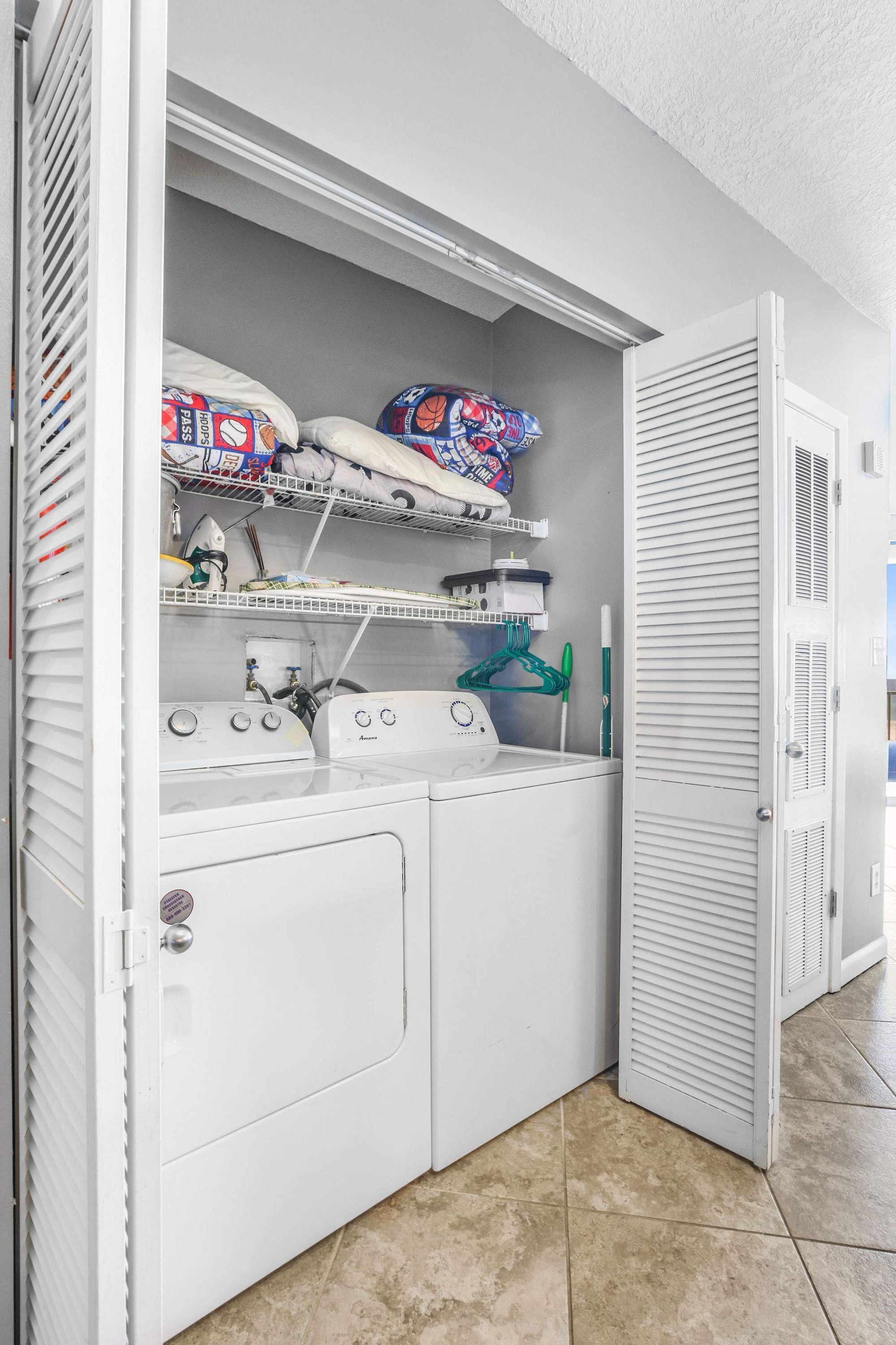 A laundry room with a washer and dryer, shelves with folded clothes, and a green hanger.