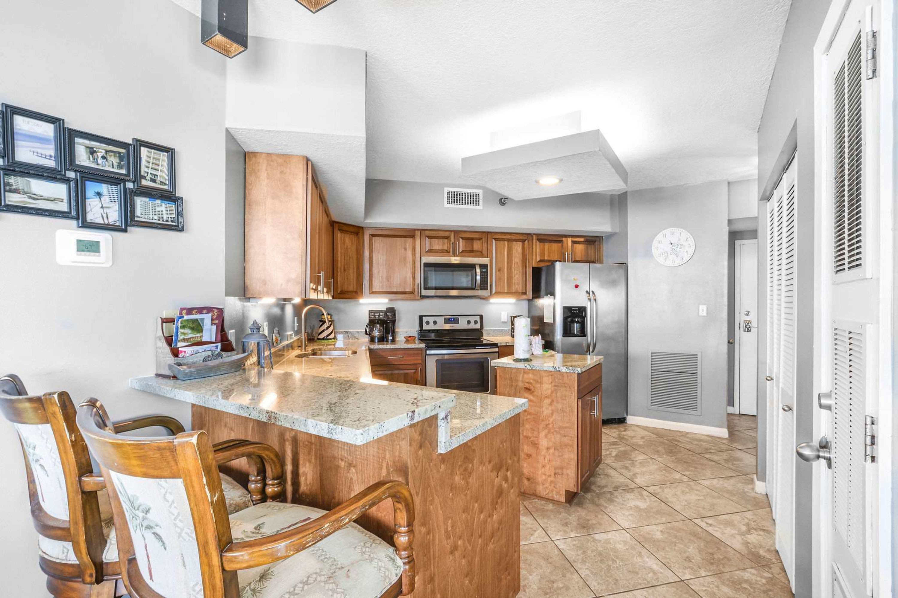 A kitchen with wooden cabinets, a microwave, a refrigerator, and a dining area with chairs.