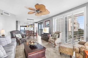 A spacious living room with a ceiling fan, a dining area, and large windows with blinds. - Pelican Pointe 301- Corner Unit 3rd Floor Gulf-front (Orange Beach)