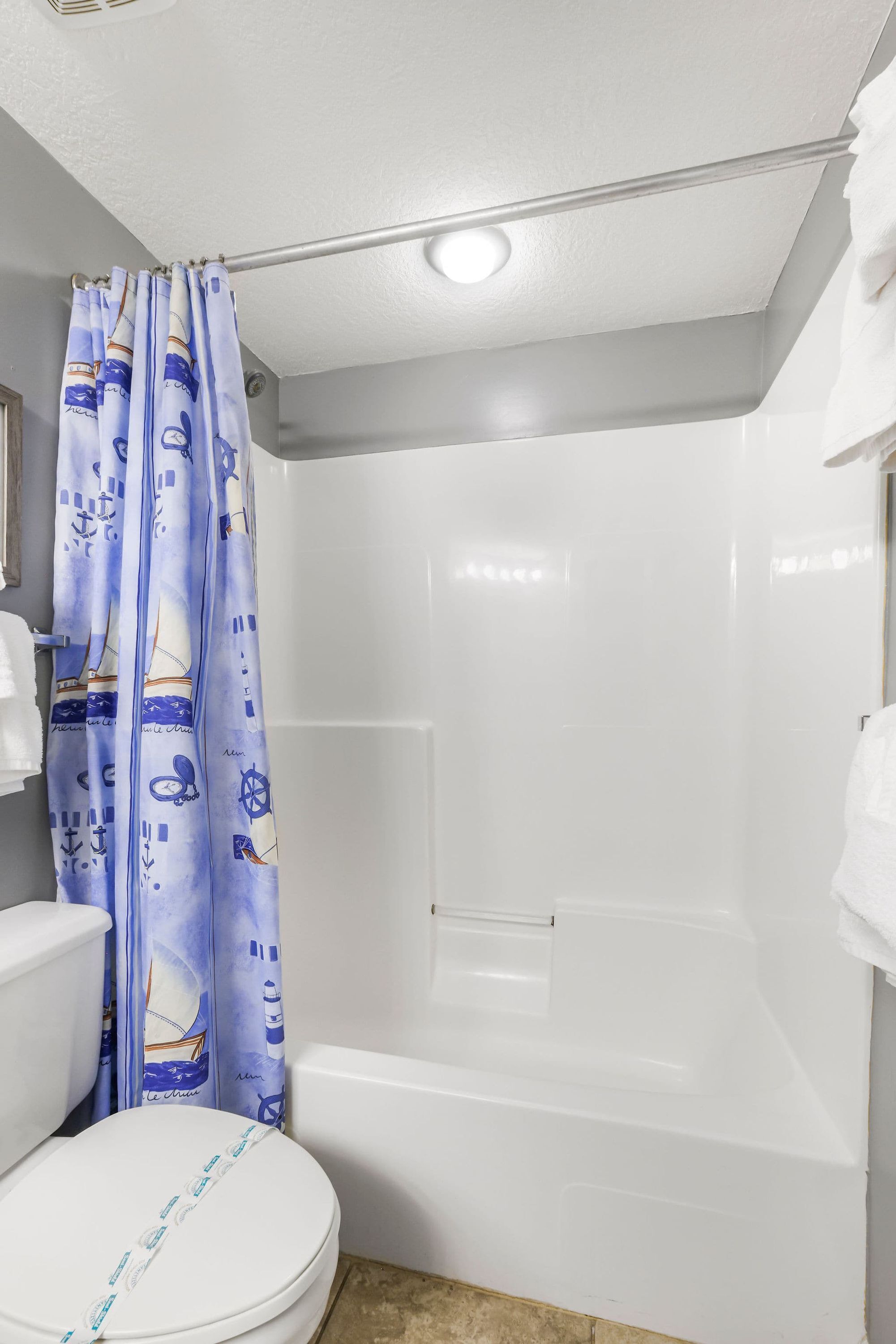 A bathroom with a white toilet, a bathtub, and a shower curtain with nautical designs.
