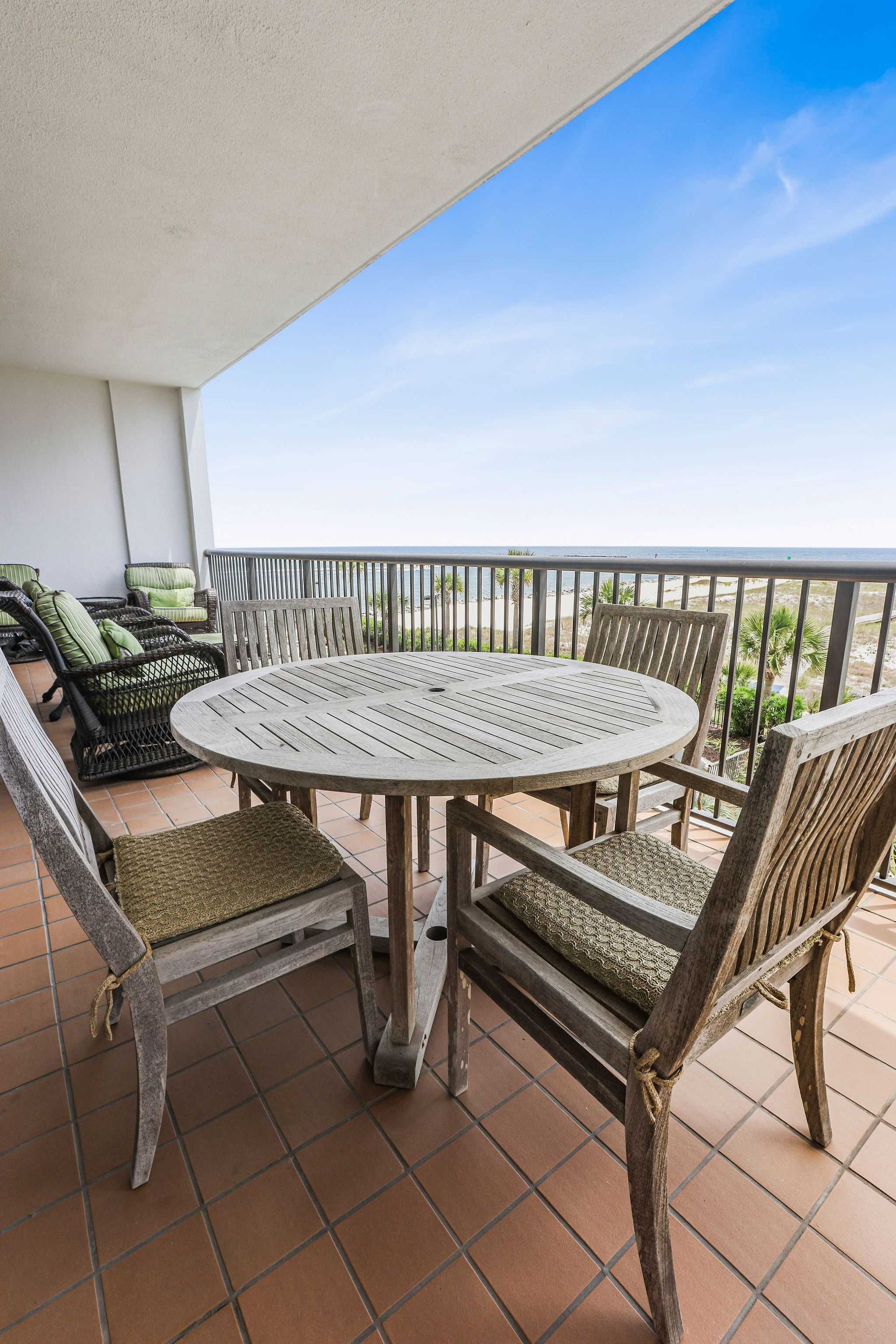 A balcony with a round wooden table and chairs, surrounded by wicker furniture.