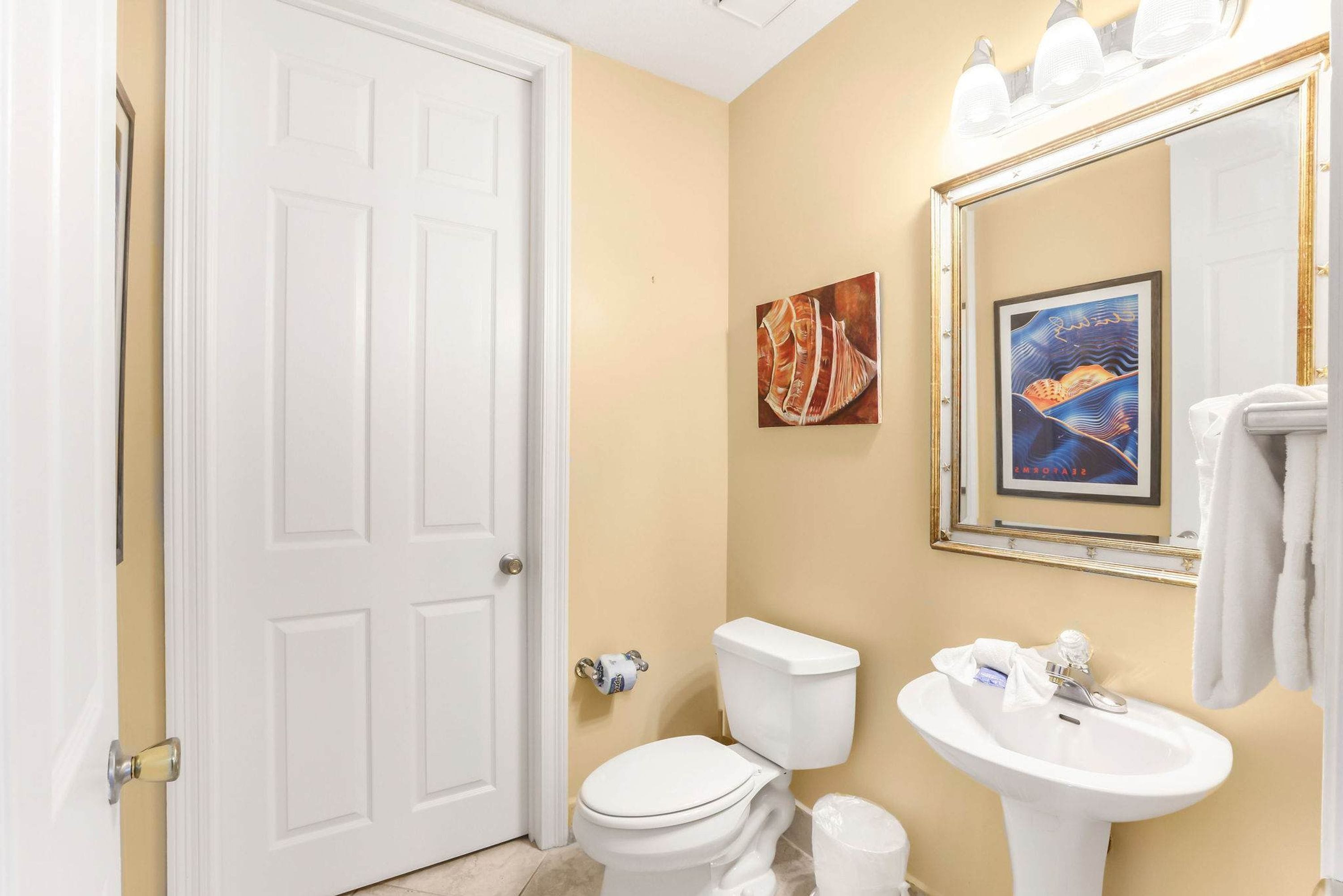A bathroom with a white toilet, a sink, and a mirror. There are two framed artworks on the wall.