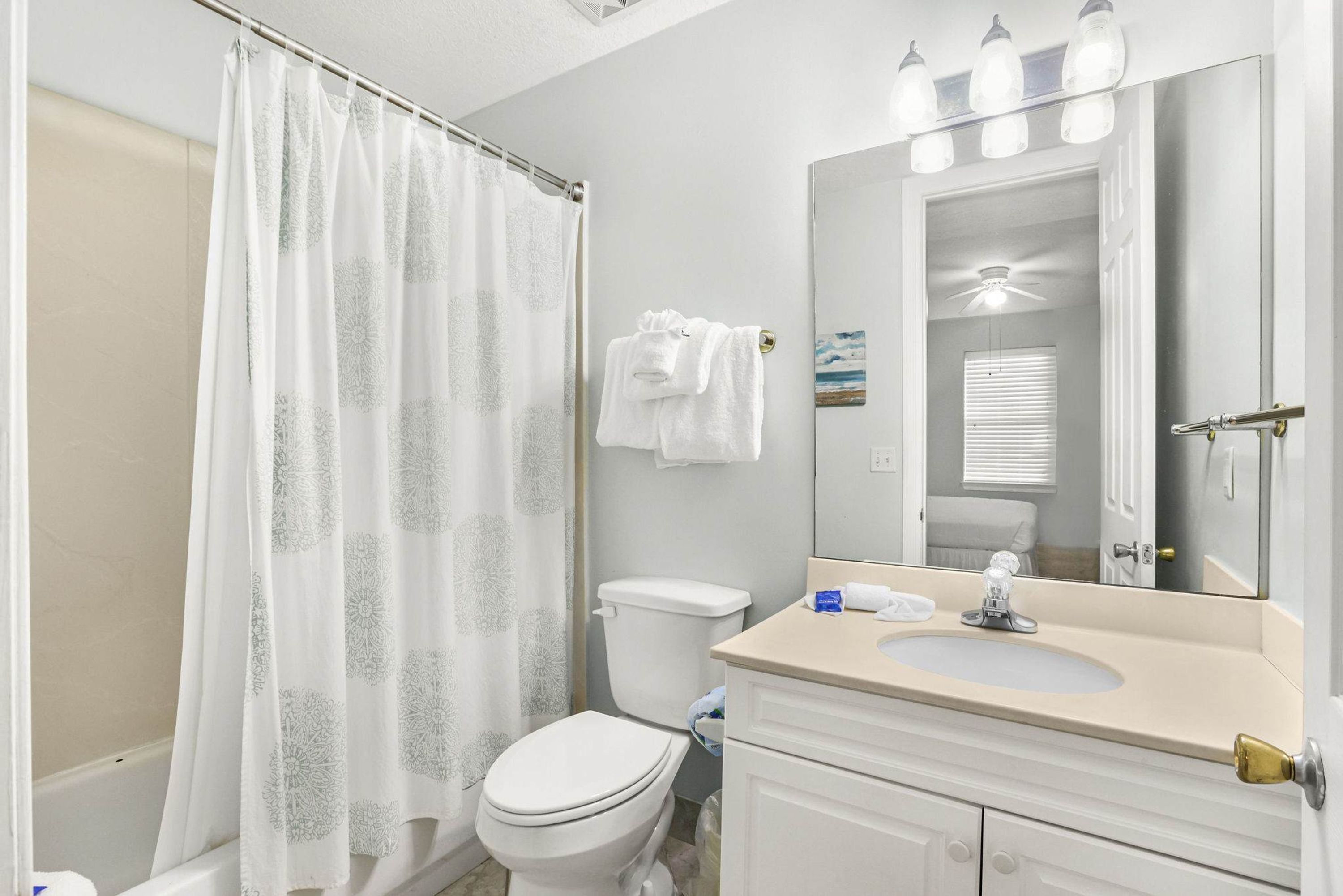 Une salle de bain équipée d’un rideau de douche, de toilettes, d’un lavabo et d’un miroir.