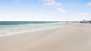 Ein Strand mit weitem, sandigen Ufer, ruhigem Wasser und blauem Himmel.