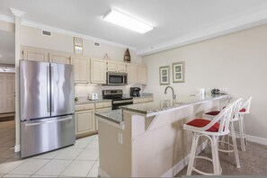 Eine Küche mit Edelstahlkühlschrank, Mikrowelle und Herd, eine Bar mit weißen Barhocker und hellem Korpus.