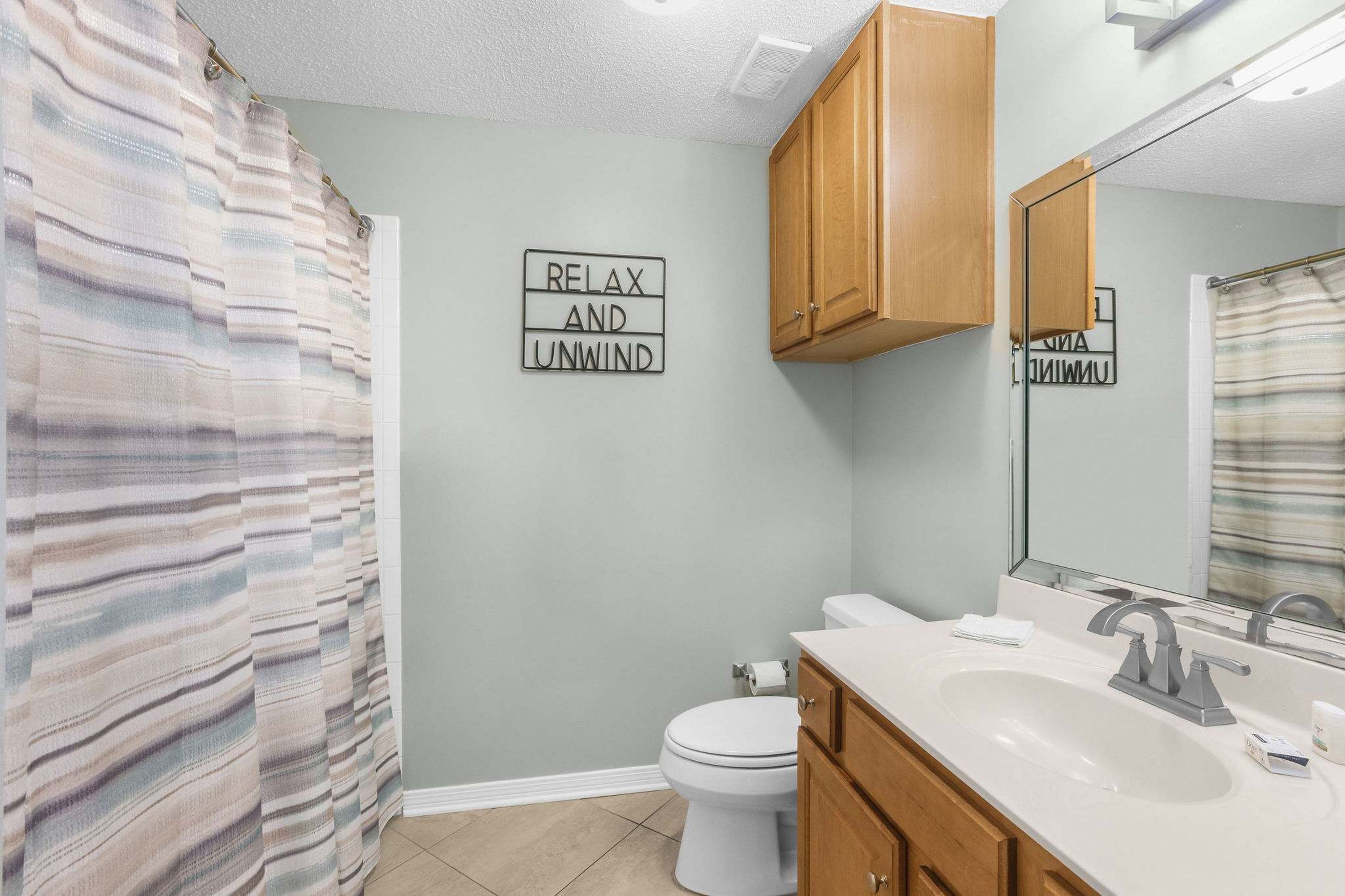 A bathroom with a toilet, sink, and wooden cabinets. A sign on the wall reads "RELAX AND UNWIND."