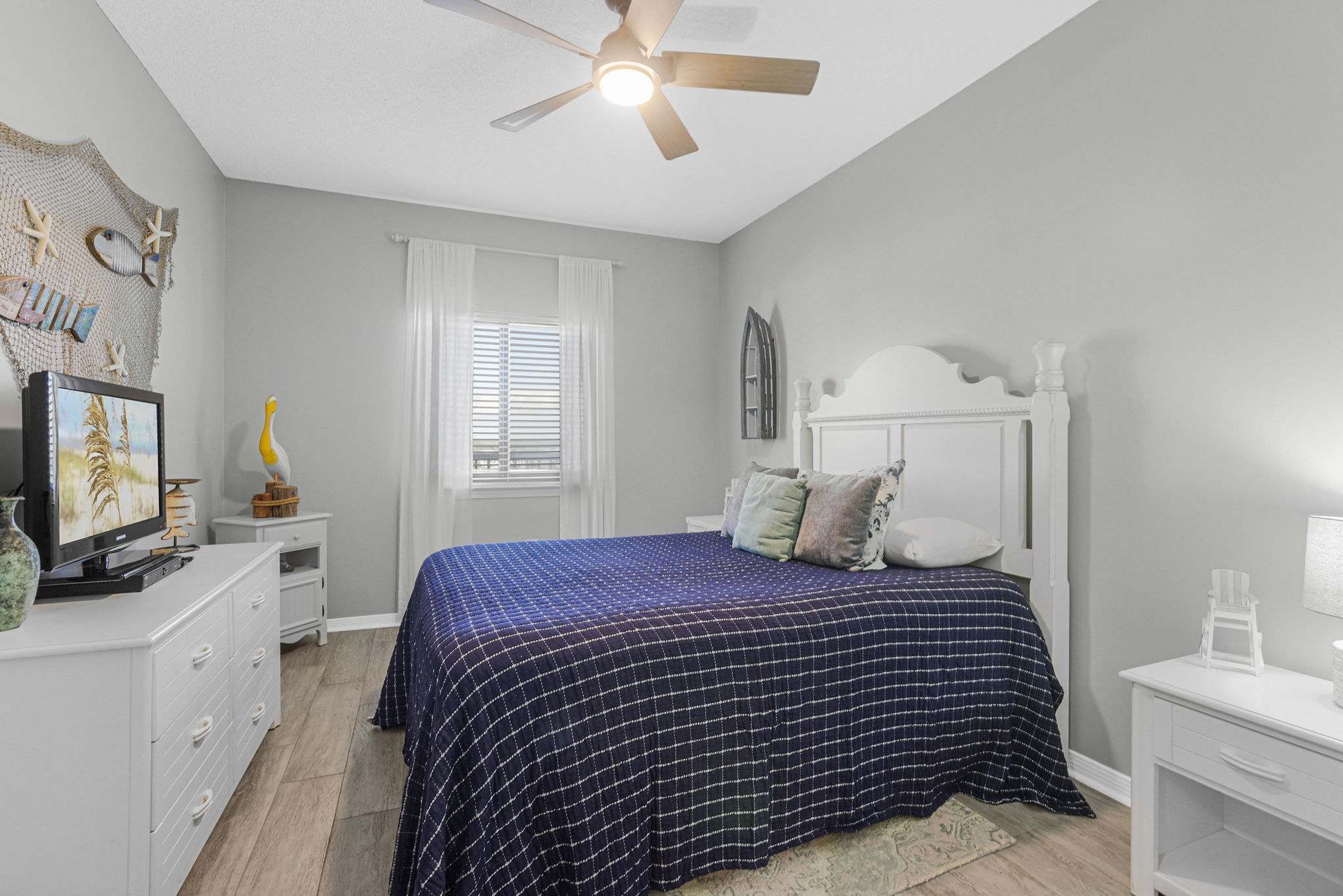 A bedroom with a bed, a ceiling fan, a dresser, a nightstand, and a window with blinds.