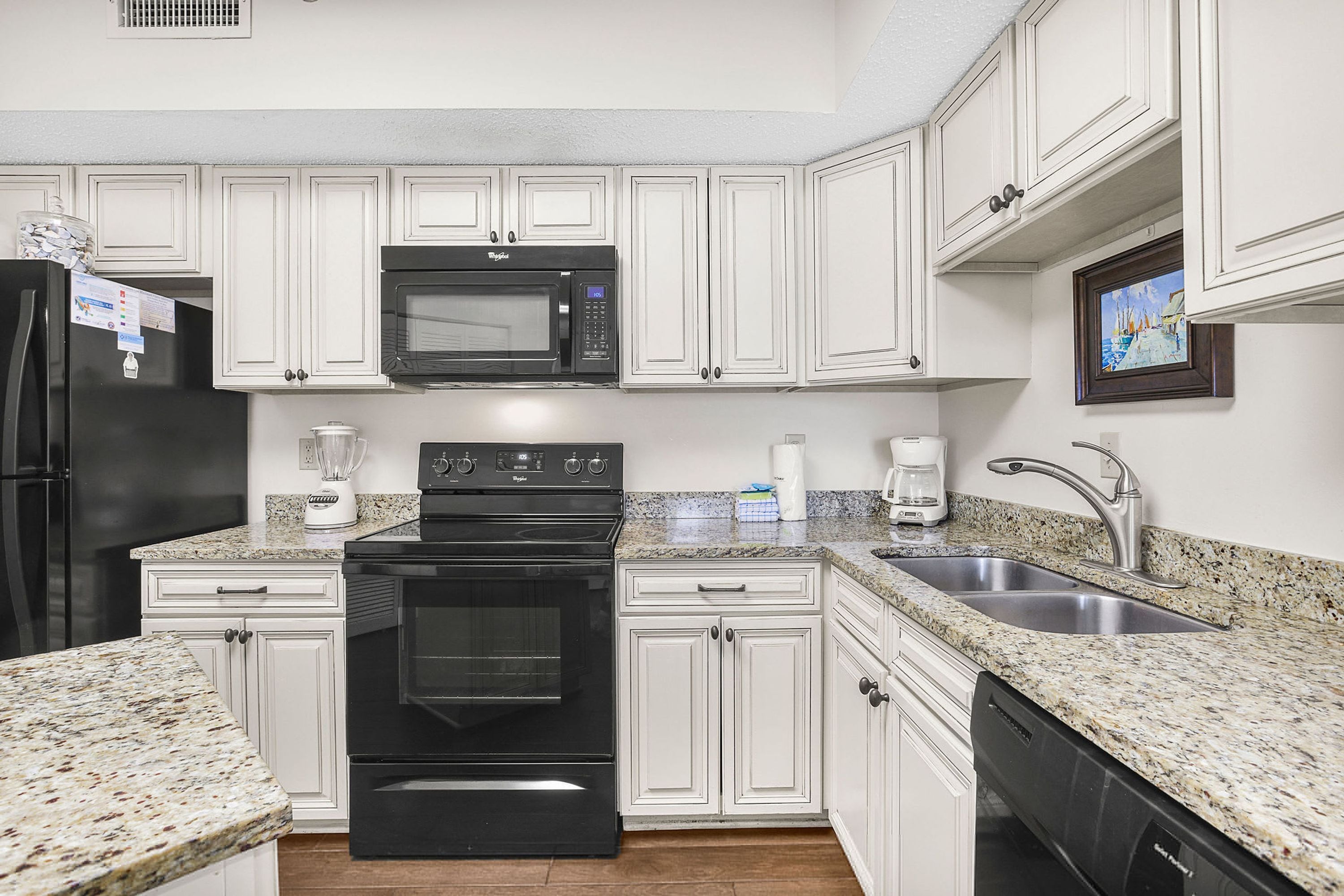 A kitchen with white cabinets, a black stove, a microwave, a sink, and a dishwasher.
