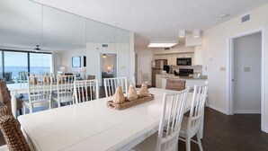 Zona pranzo moderna con tavolo e sedie bianche, una cucina sullo sfondo e un grande specchio che riflette l'ambiente.