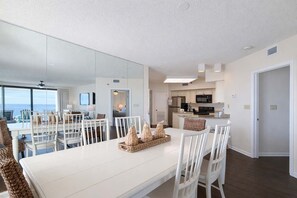 Ein moderner Essbereich mit einem weißen Tisch und Stühlen, eine Küche im Hintergrund und ein großer Spiegel, der den Raum widerspiegelt.