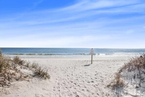 A sandy beach with a signpost in the distance, leading to the ocean. - Don t Worry Beach House 3 2 2 Blocks to Beach (Gulf Shores)