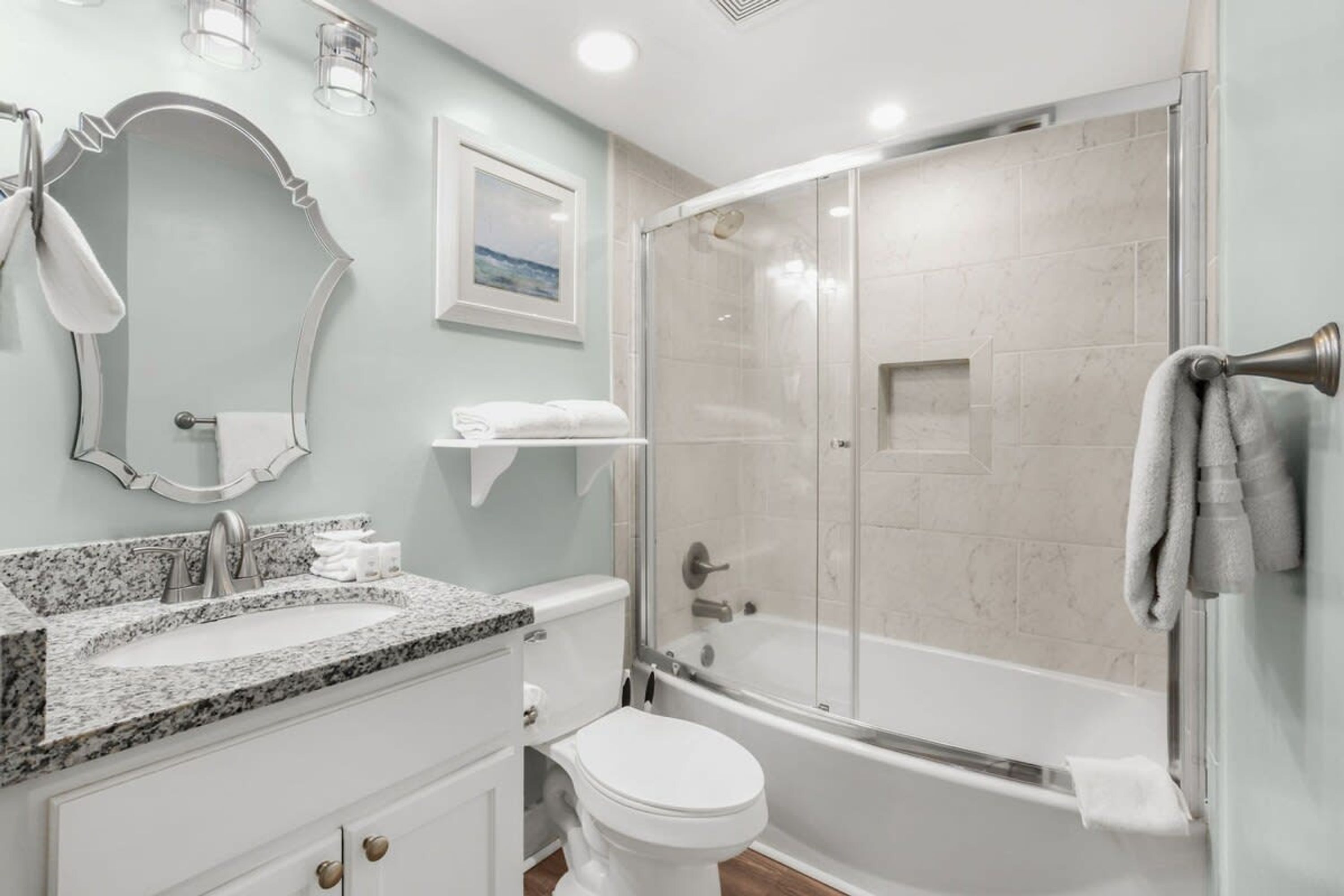 A modern bathroom with a granite countertop sink, a toilet, a glass-enclosed shower, and a bathtub.