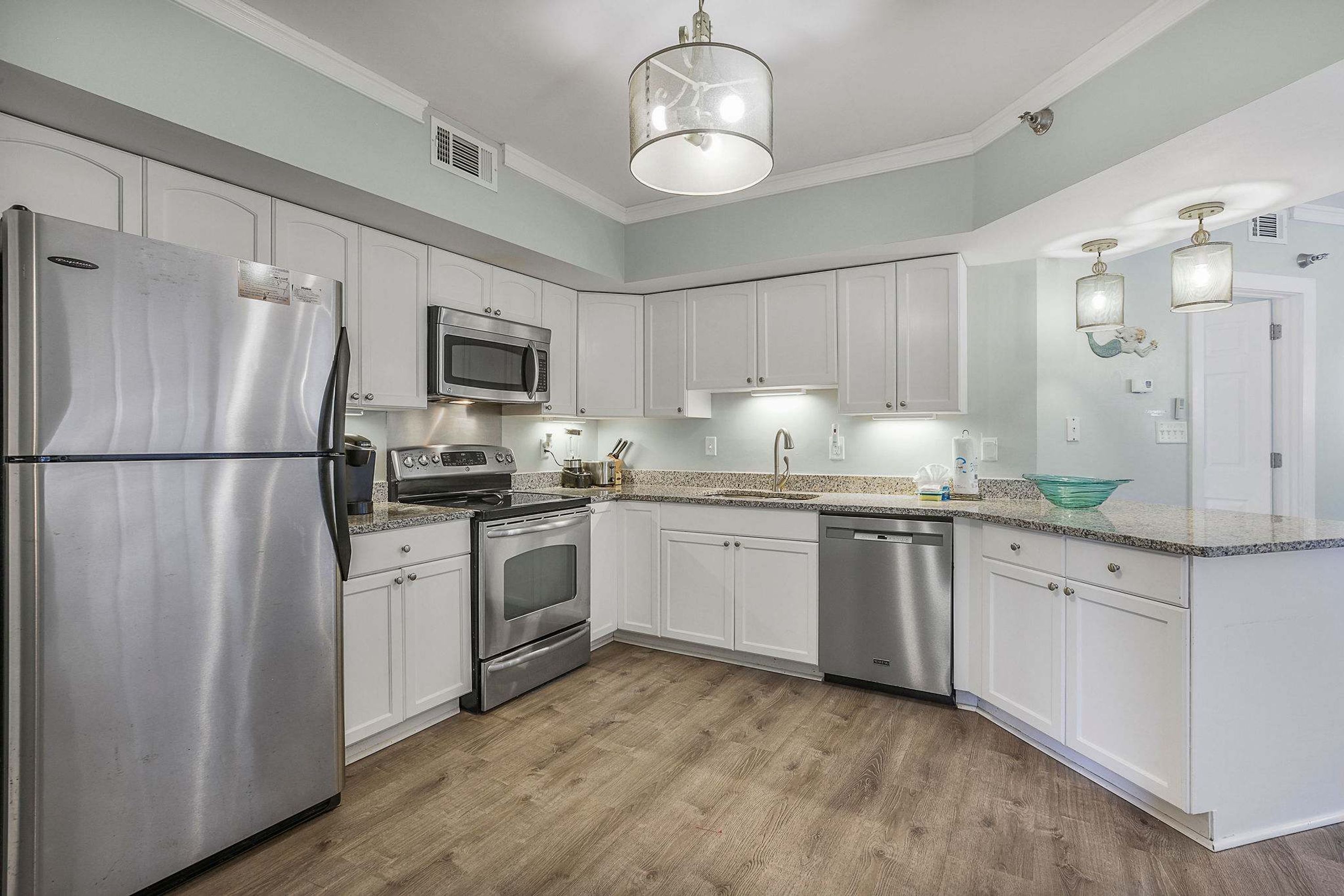 A modern kitchen with white cabinets, stainless steel appliances, and a wooden floor.