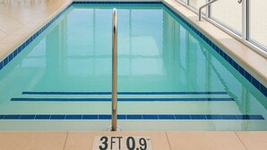 En indendørs swimmingpool med udsigt til stranden, et redningsbassin og et opholdsområde med stole.