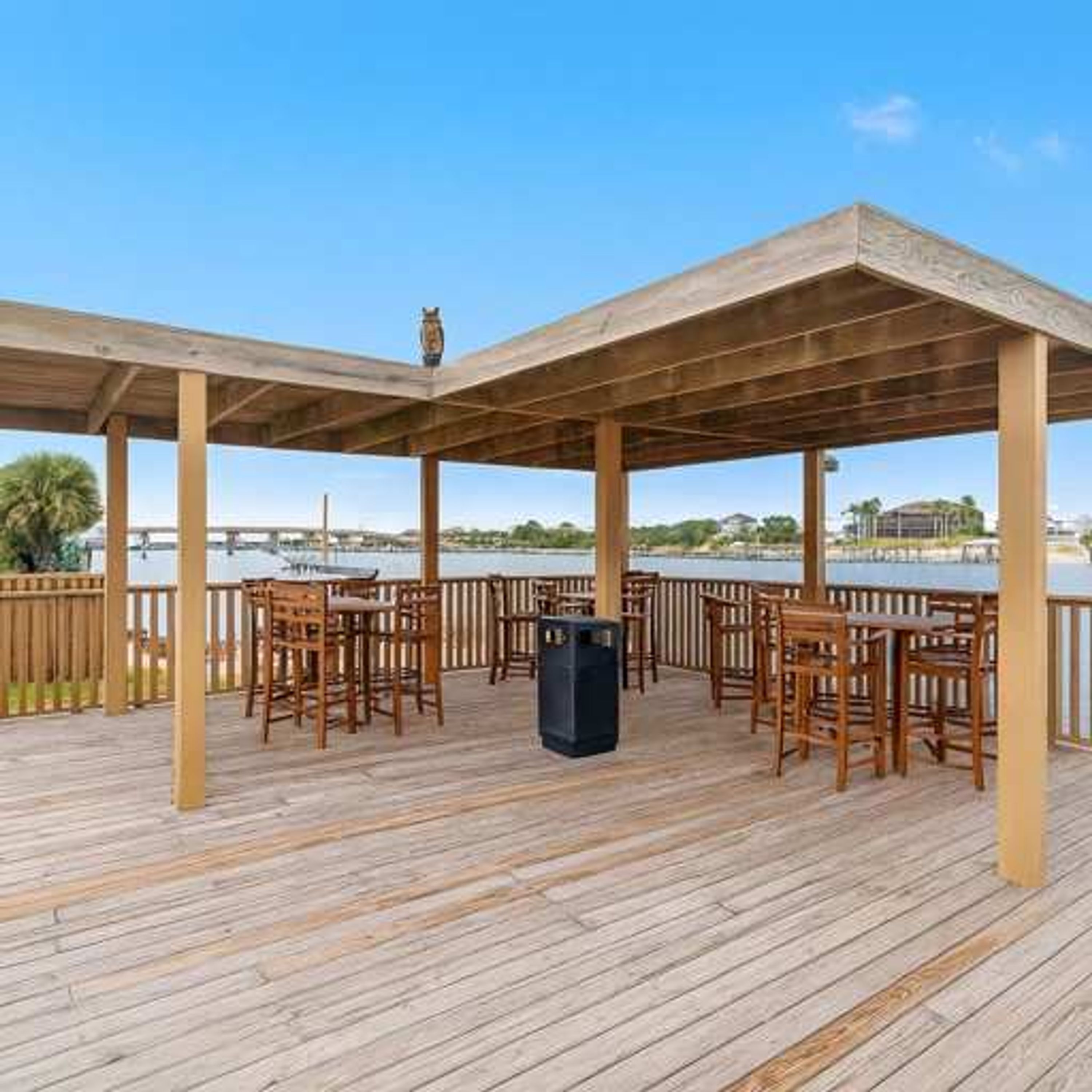 Terraza de madera al aire libre con mesas y sillas, con vista a un cuerpo de agua.