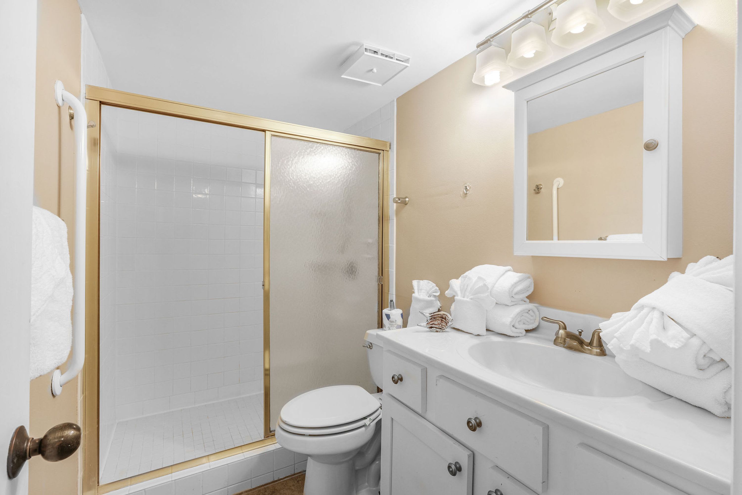 A bathroom with a glass shower enclosure, a white toilet, a vanity with a sink, and a mirror.